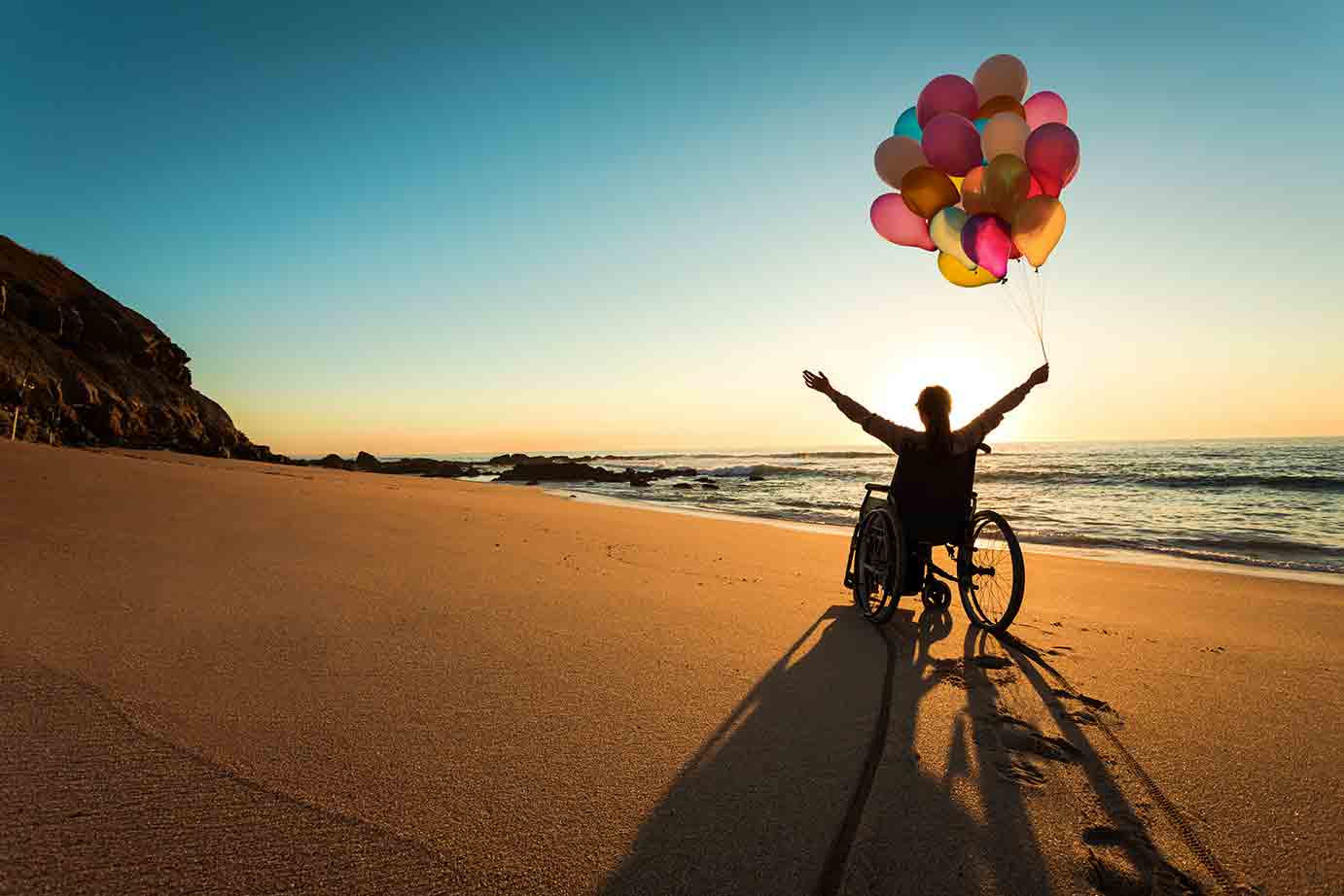 Woman in a wheelchair on a beach with balloons